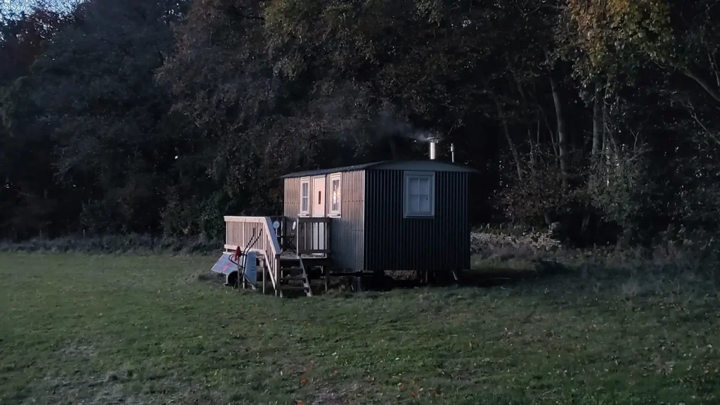 A black metal shepherd's hut for airbnb nestled next to old forest on Eastleach Downs Organic Farm land