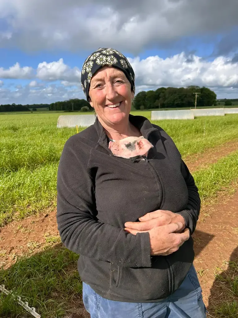 Your host, Nell, holding a piglet in her jacket at Eastleach Downs Organic Farm Shepherd's Hut, Gloucestershire