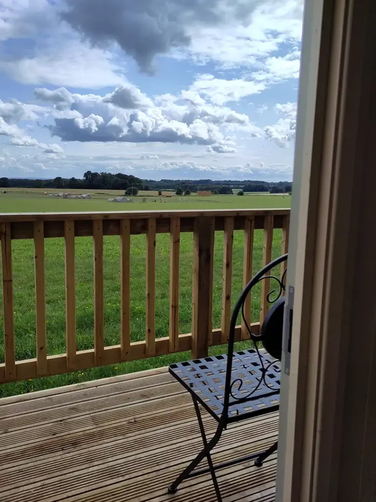 The veranda's view, looking over rolling fields, at Eastleach Downs Organic Farm Shepherd's Hut, Gloucestershire
